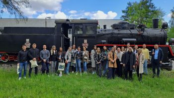 Goście z Uniwersytetu Josip Juraj Strossmayer w Osijku oraz przedstawiciele Łukasiewicz - PIT stoją przed zabytkową lokomotywą