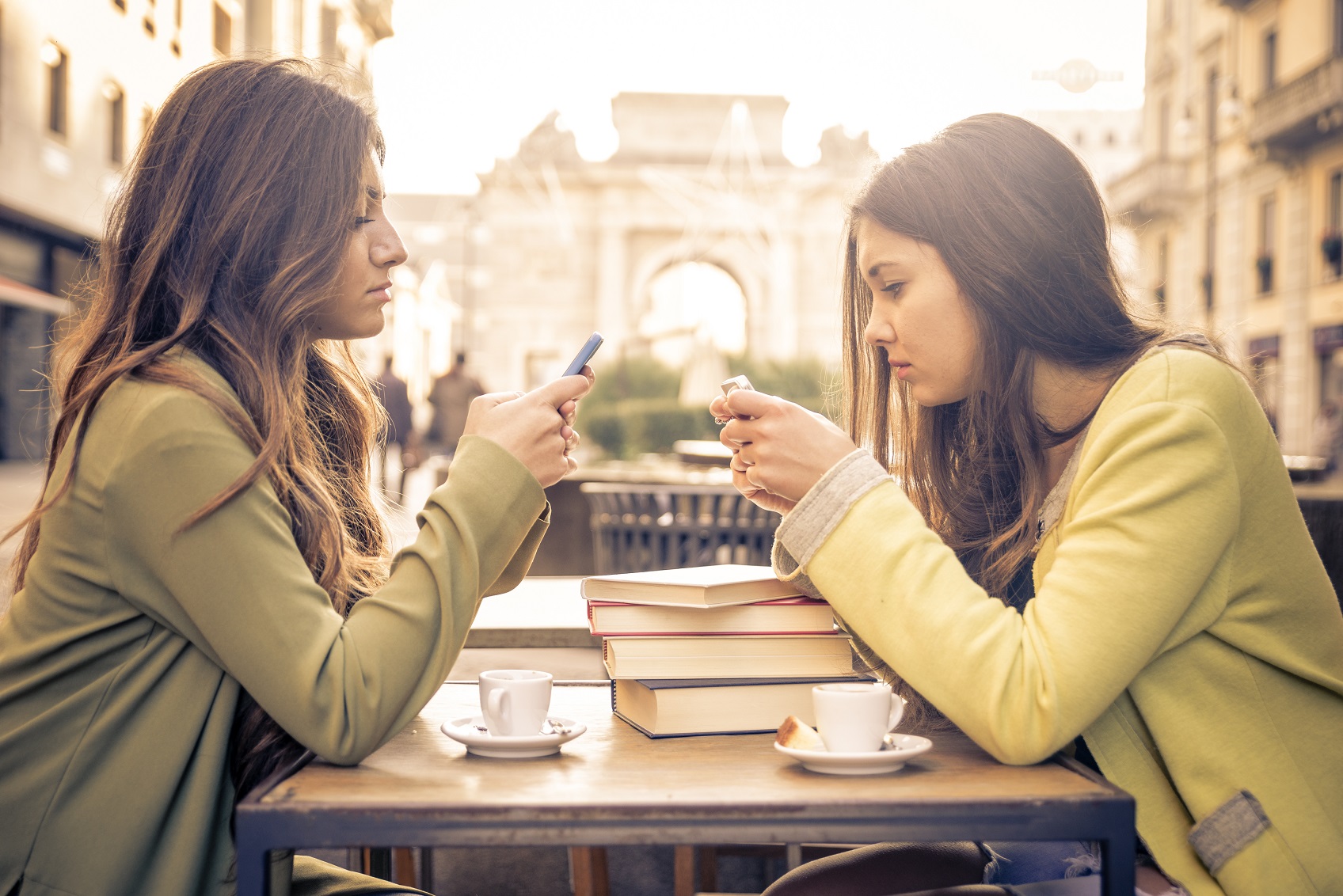 dwie młode kobiety wpatrzone we smatfony w tle włoskie miasto