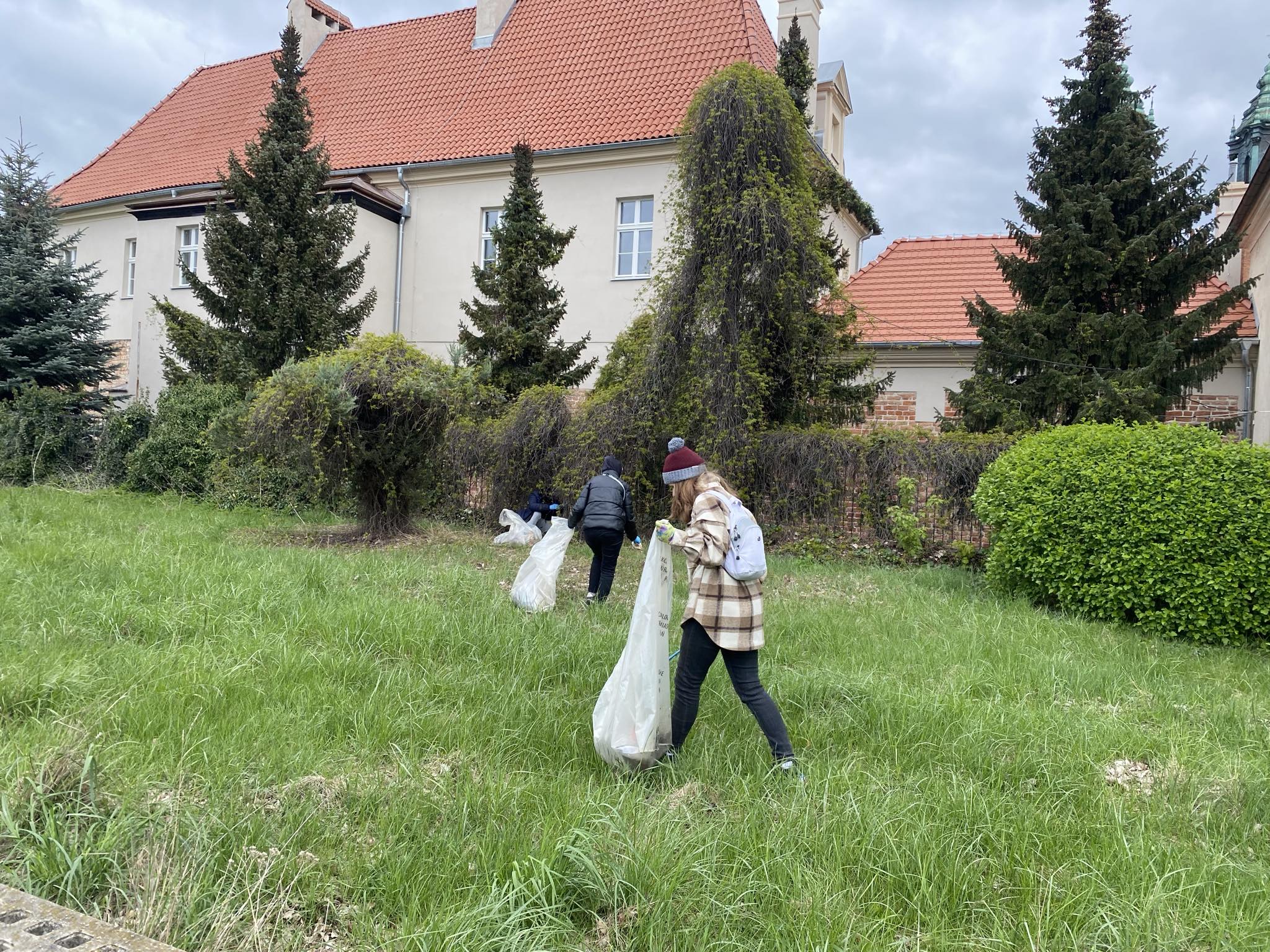 Trzy osoby na trawniku zbierają śmieci do worków