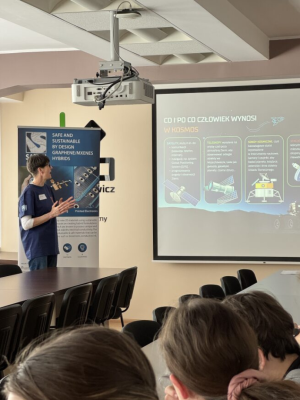 Badaczka wskazuje na tablicę i opowiada o materiałach