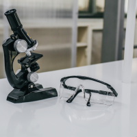 Mikroskop optyczny i okulary ochronne na białym stole laboratoryjnym