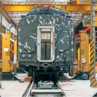 Diagnostyka techniczna wagonu pasażerskiego w nowoczesnej bazie utrzymaniowo-naprawczej Szary wagon kolejowy podczas przeglądu technicznego między żółtymi podnośnikami w hali serwisowej